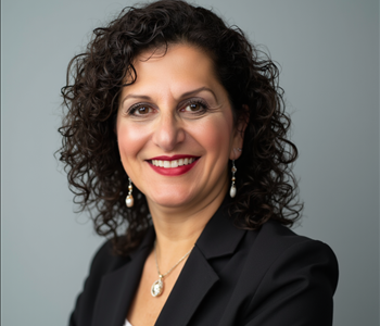 Woman with black curly hair in a black blazer and white blouse