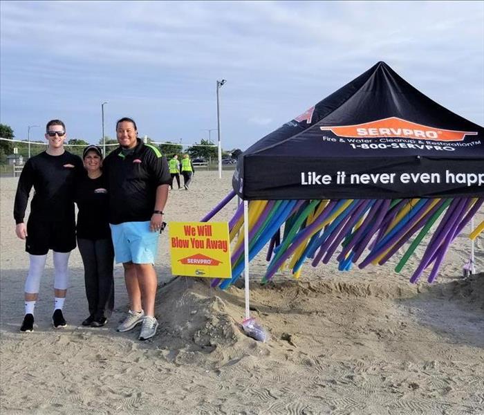 3 people standing in front of a servpro tent with obstacle course on the beach