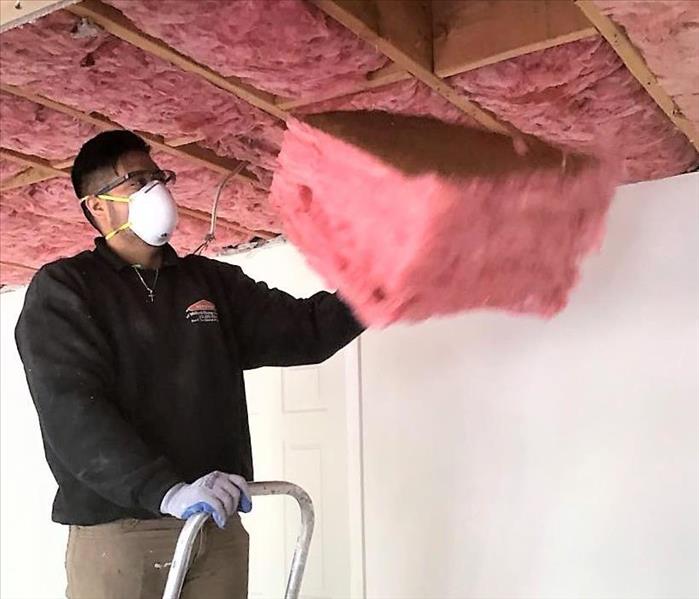 man on a ladder removing wet insulation from ceiling