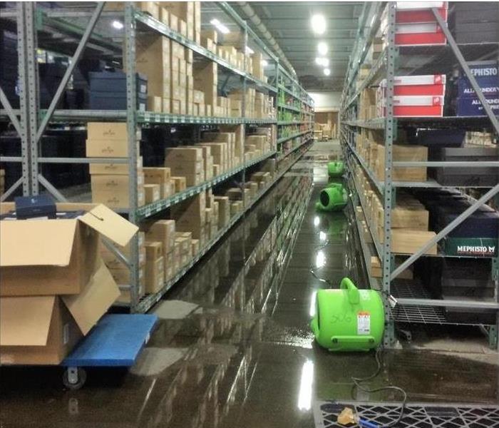 a flooded warehouse with shelving and servpro dehumidifiers on the floor