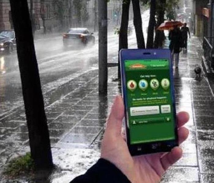 a hand holding a phone with a SERVPRO app on it on a rainy street